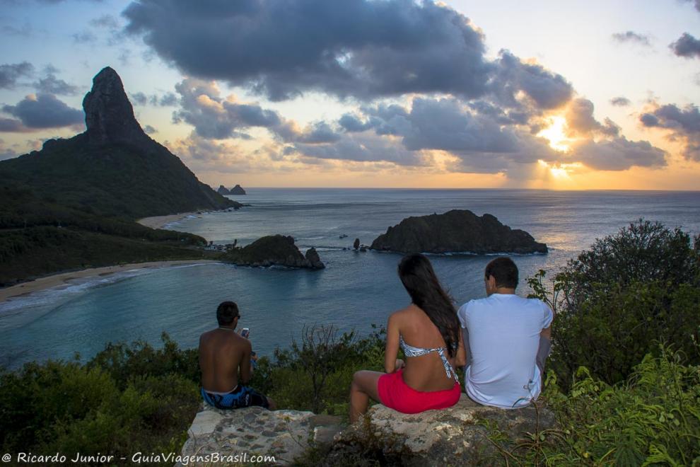Imagem de turistas sentados nas pedras admirando por do sol.